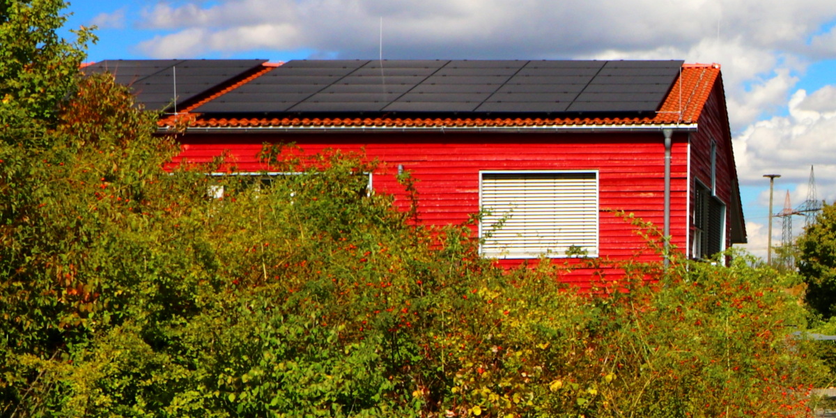 Ein rotes Haus hinter Büschen mit einer Dachsolaranlage